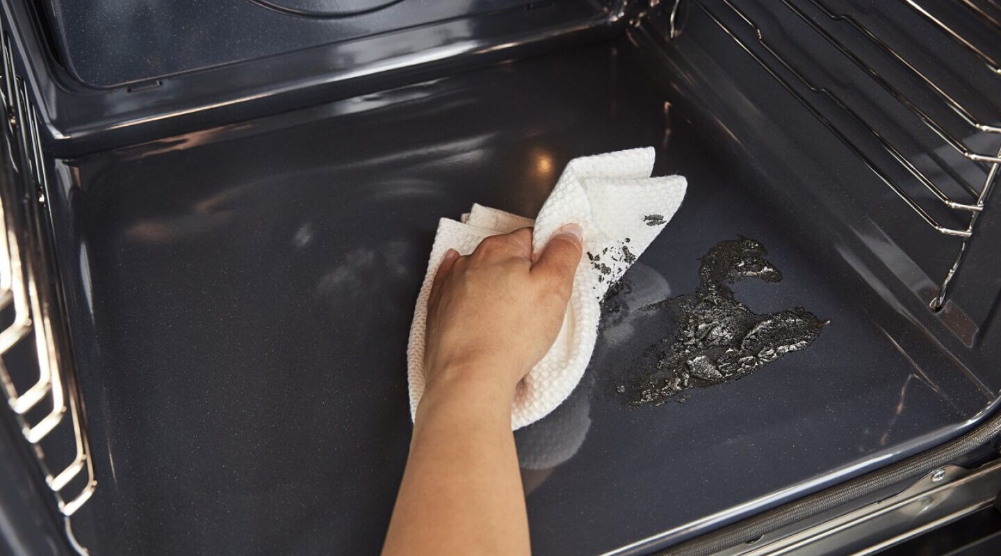Hand wiping away grime from the bottom of an oven Hand wiping away grime from the bottom of an oven