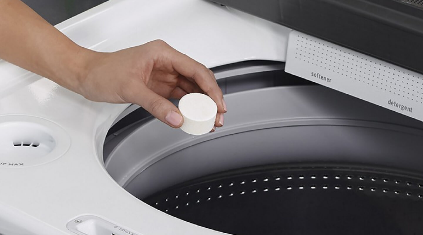Hand putting a cleaning tablet into a washing machine Hand putting a cleaning tablet into a washing machine