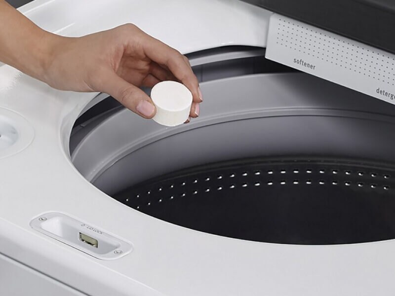 Hand putting a cleaning tablet into a washing machine Hand putting a cleaning tablet into a washing machine
