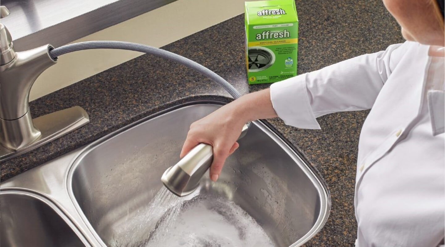 A person cleaning their sink disposal with affresh® garbage disposal cleaner tablets