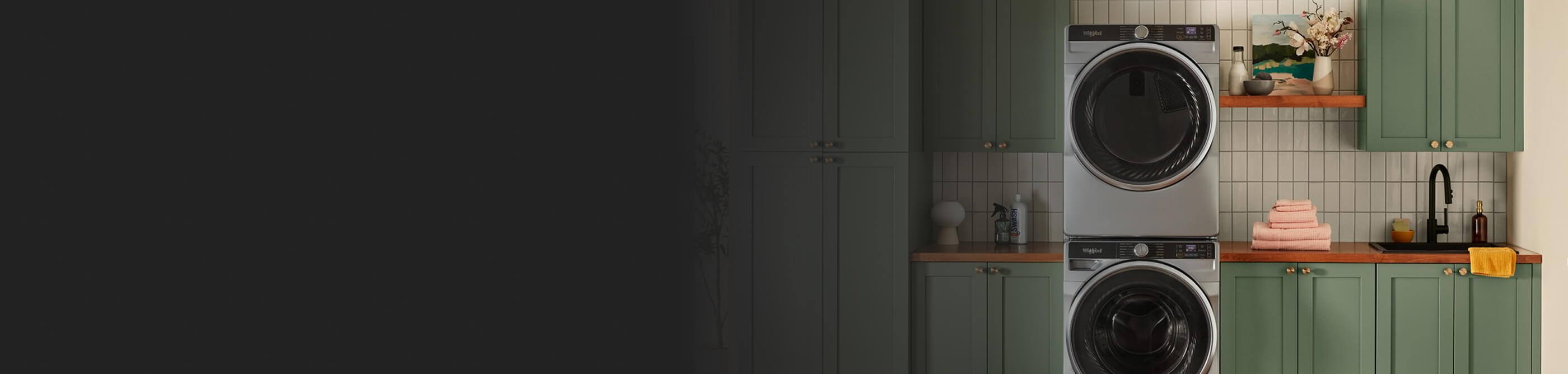 A stainless steel stackable washer and dryer in a laundry room with green cabinetry