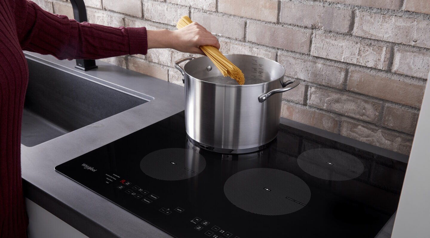 Person adding pasta to a pot on an induction cooktop