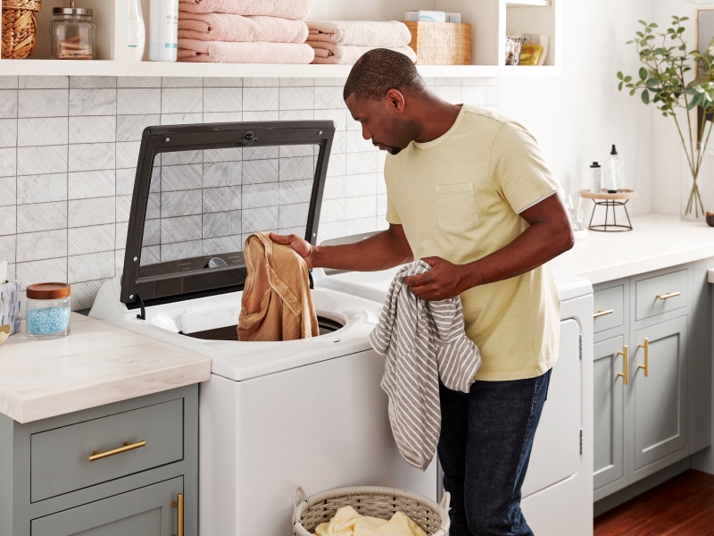 Person loading laundry into a top load washing machine Person loading laundry into a top load washing machine load washer