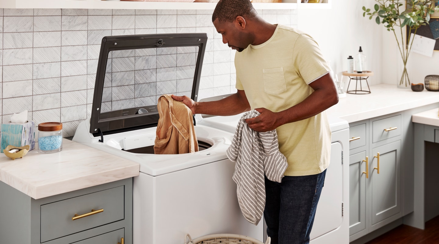 Person loading laundry into a top load washing machine Person loading laundry into a top load washing machine