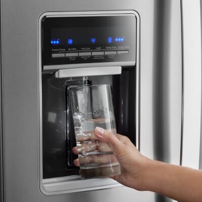 A person filling their glass from a refrigerator water dispenser