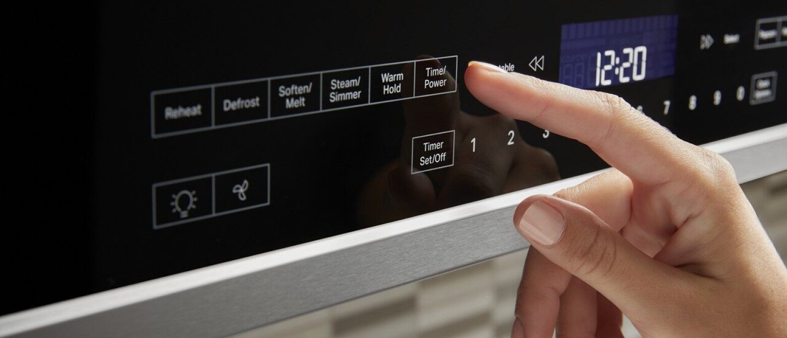 Hand touching microwave control panel