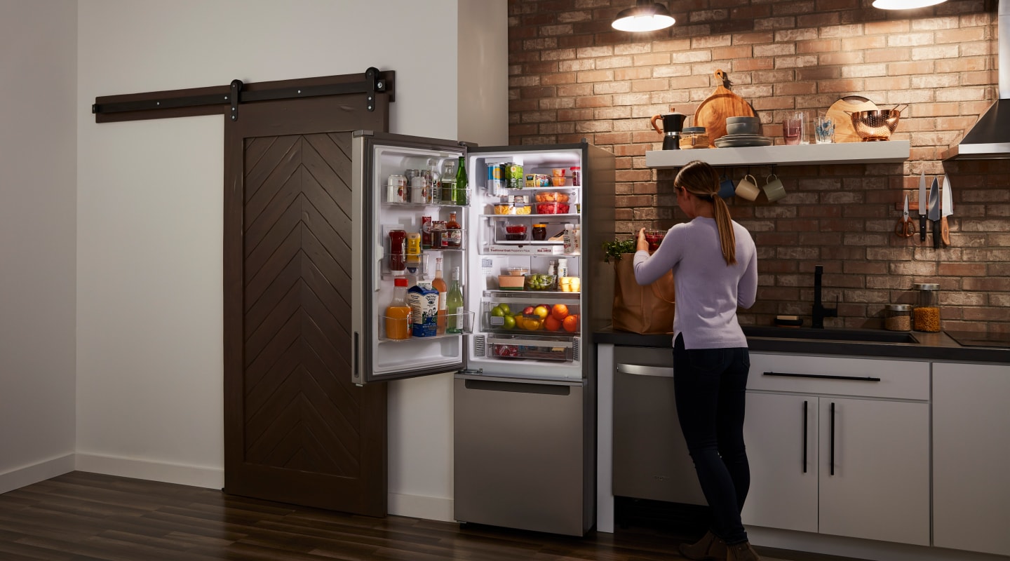 Woman standing in front of an open stainless steel Whirlpool® bottom freezer fridge Woman standing in front of an open stainless steel Whirlpool® bottom freezer fridge