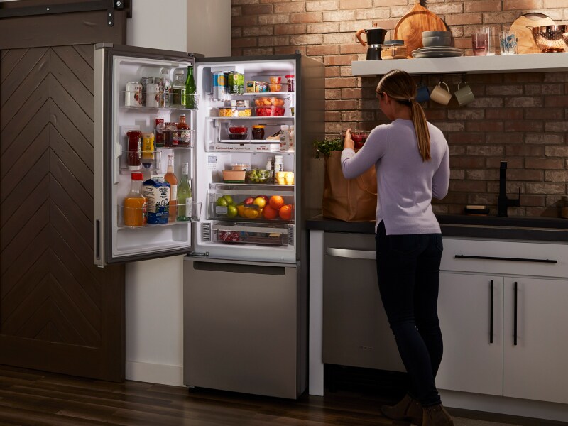 Woman standing in front of an open stainless steel Whirlpool® bottom freezer fridge Woman standing in front of an open stainless steel Whirlpool® bottom freezer fridge