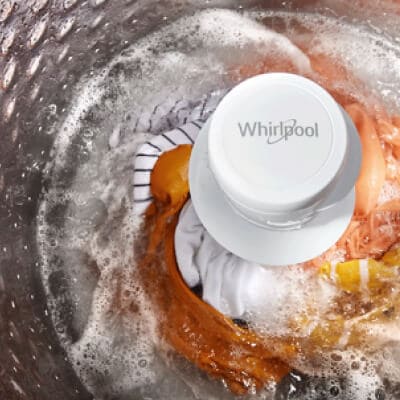 Interior of a Whirlpool® Washer with an agitator washing orange, white and yellow garments
