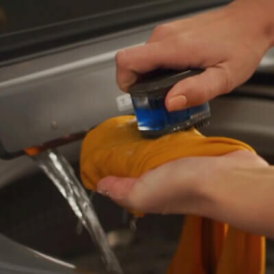 Close up of a person using a pretreat brush to spot treat odor on a garment