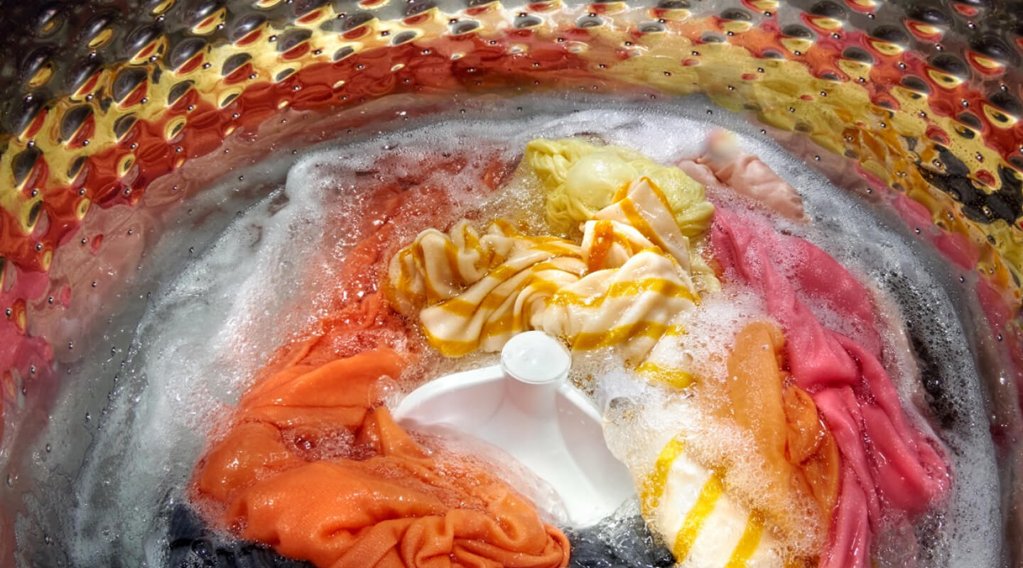 Interior of a Whirlpool® Washer with an impeller washing yellow, orange, pink, gray and white garments Interior of a Whirlpool® Washer with an impeller washing yellow, orange, pink, gray and white garments