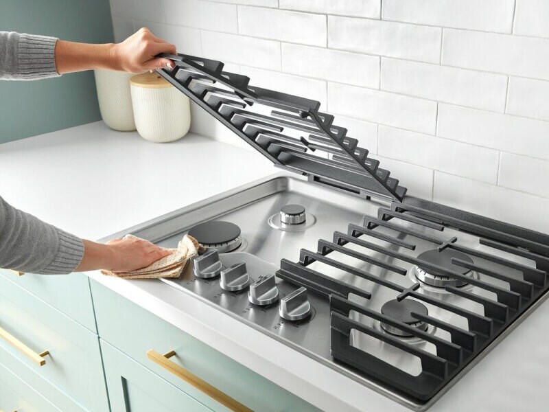 Person lifting the grate on a gas cooktop Person lifting the grate on a gas cooktop