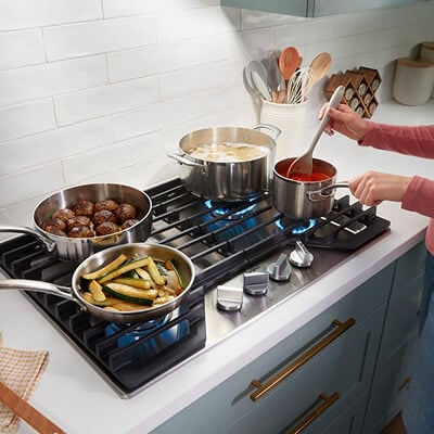 Four dishes cooking on edge-to-edge grates of gas cooktop