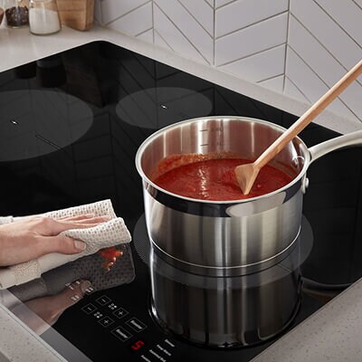 Person wiping spaghetti sauce splatter from ceramic glass cooktop surface