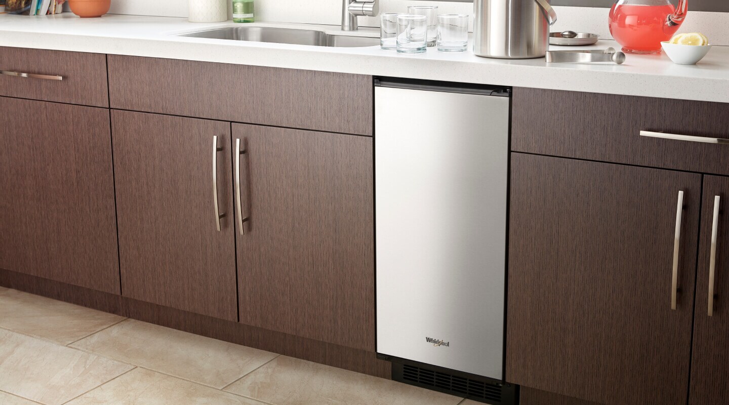 A Whirlpool® Icemaker installed amid brown cabinetry