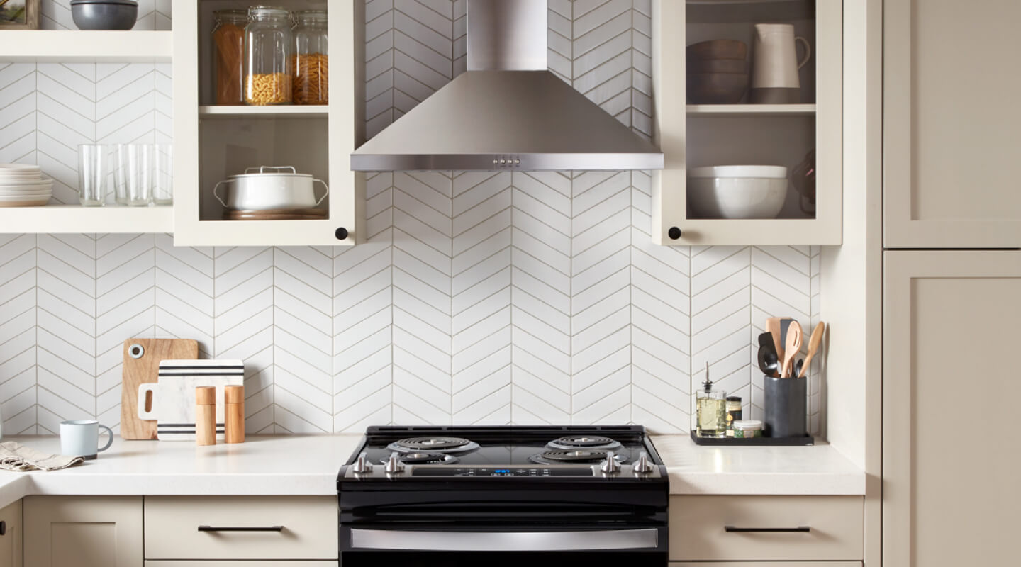 A Whirlpool® Chimney Wall Mount Range Hood and Range in a kitchen