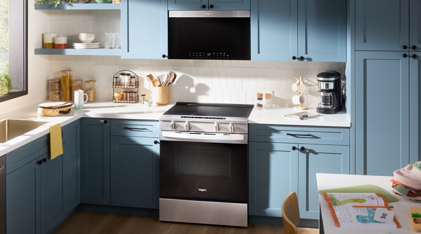 An over-the-range microwave above an electric slide-in range inside a kitchen with blue cabinets