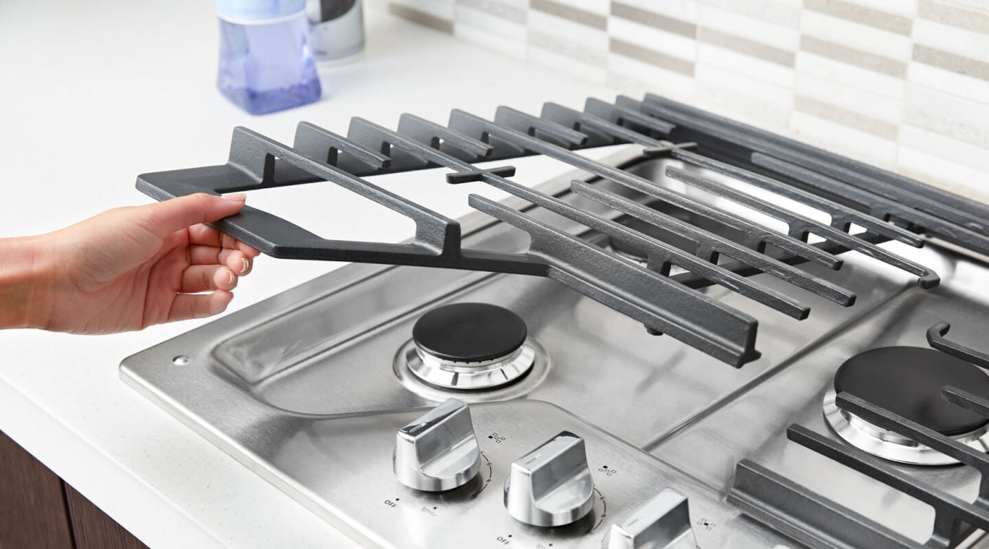 Person placing grates back on a gas cooktop Person placing grates back on a gas cooktop