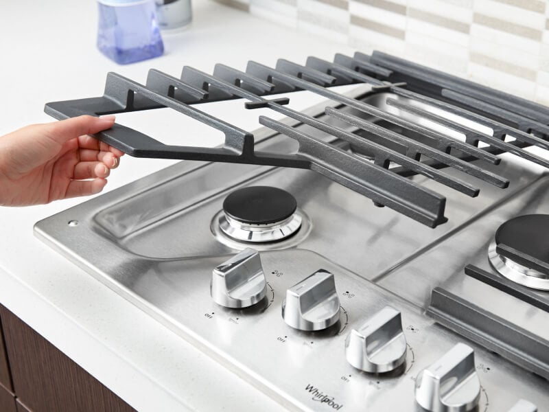 Person placing grates back on a gas cooktop Person placing grates back on a gas cooktop