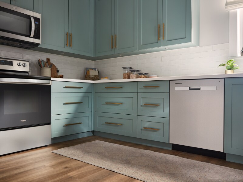 A Whirlpool® dishwasher and range in a modern kitchen with teal cabinets. A Whirlpool® dishwasher and range in a modern kitchen with teal cabinets.