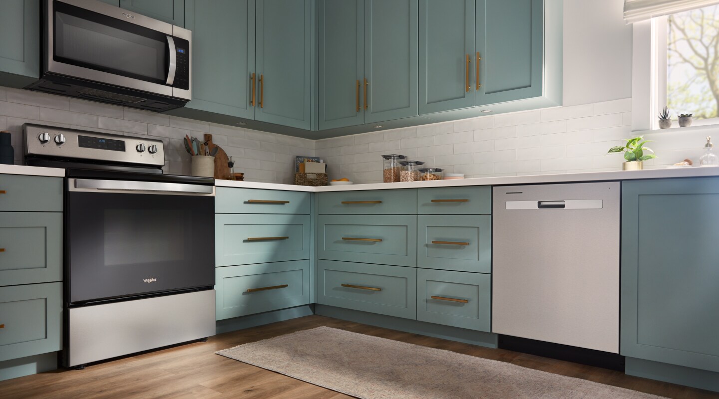 A Whirlpool® dishwasher and range in a modern kitchen with teal cabinets. A Whirlpool® dishwasher and range in a modern kitchen with teal cabinets.