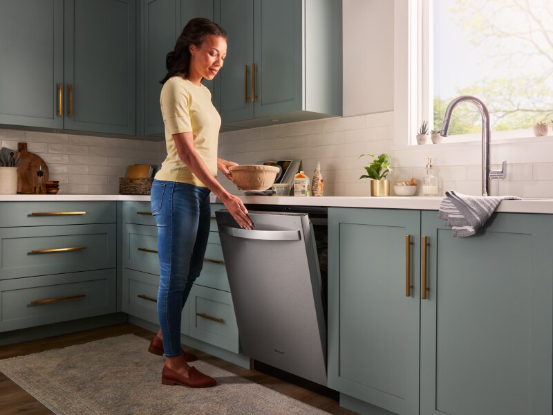 A person closing a stainless steel dishwasher surrounded by teal cabinetry. A person closing a stainless steel dishwasher surrounded by teal cabinetry.
