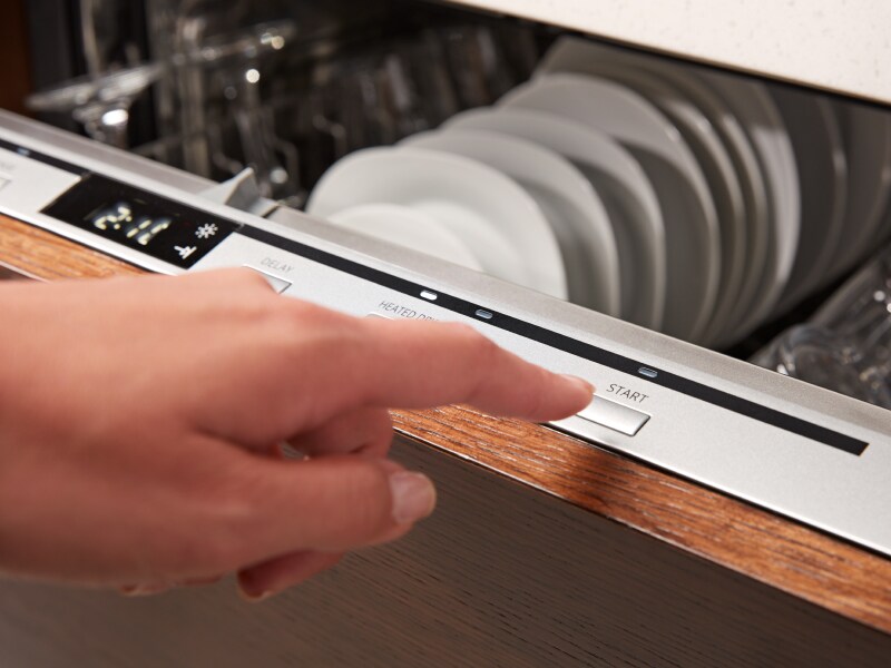 A person starting a dishwasher cycle on a top control panel. A person starting a dishwasher cycle on a top control panel.