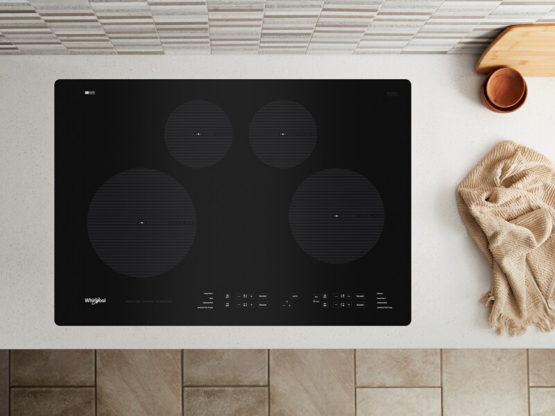 A black Whirlpool® cooktop next to various kitchen items A black Whirlpool® cooktop next to various kitchen items