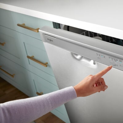 An arm pointing to the control panel on a slightly ajar semi-integrated dishwasher