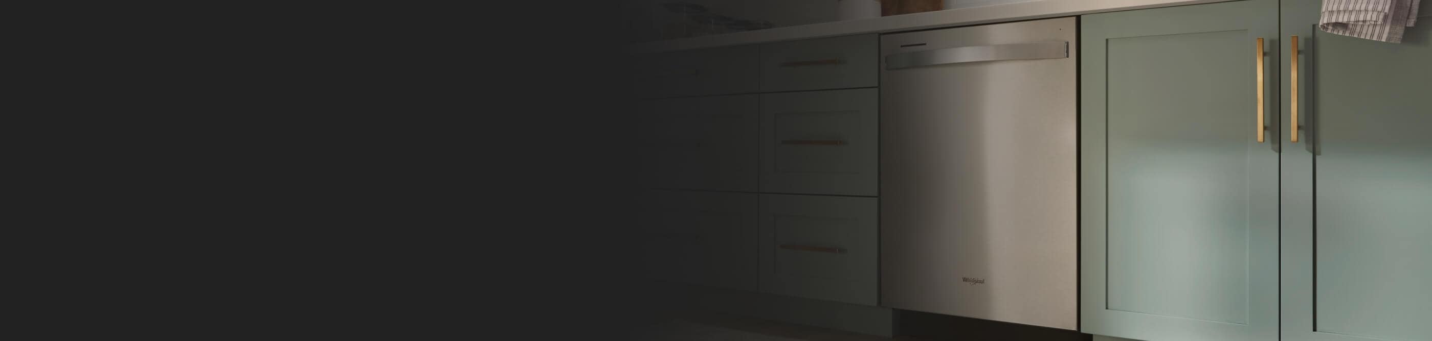 A Whirlpool® Built-In Dishwasher with Top Control and a towel handle placed between green cabinets and under white countertops