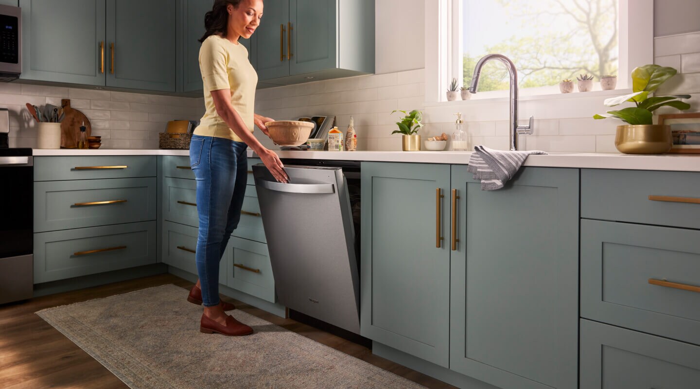 A person opening a Whirlpool® Built-In Dishwasher with Top Control and a towel handle in a kitchen with sea green cabinets and white countertops A person opening a Whirlpool® Built-In Dishwasher with Top Control and a towel handle in a kitchen with sea green cabinets and white countertops