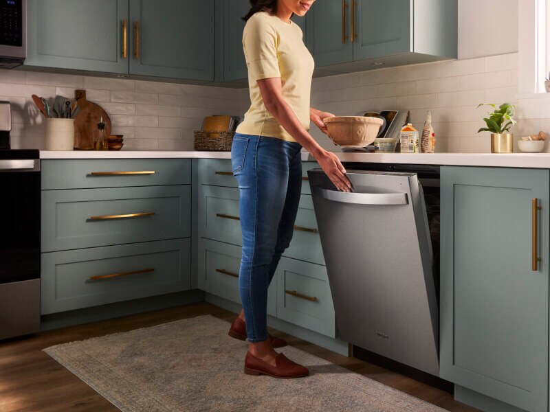 A person opening a Whirlpool® Built-In Dishwasher with Top Control and a towel handle in a kitchen with sea green cabinets and white countertops A person opening a Whirlpool® Built-In Dishwasher with Top Control and a towel handle in a kitchen with sea green cabinets and white countertops