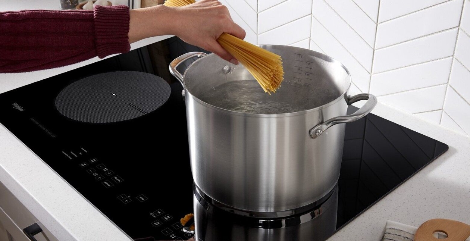 A hand putting spaghetti into pot of boiling water on a Whirlpool® Induction Cooktop A hand putting spaghetti into pot of boiling water on a Whirlpool® Induction Cooktop