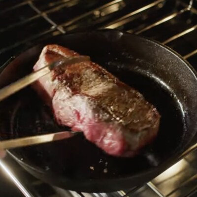 A pair of tongs arranging a steak on a skillet