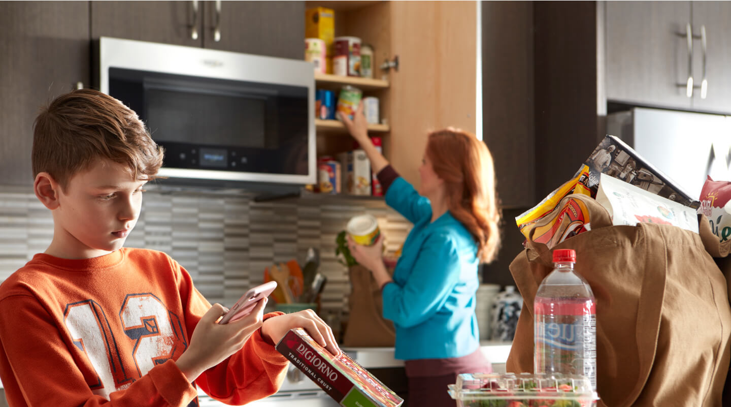 A person scanning a pizza box barcode while a person in the background puts items in the cabinet A person scanning a pizza box barcode while a person in the background puts items in the cabinet