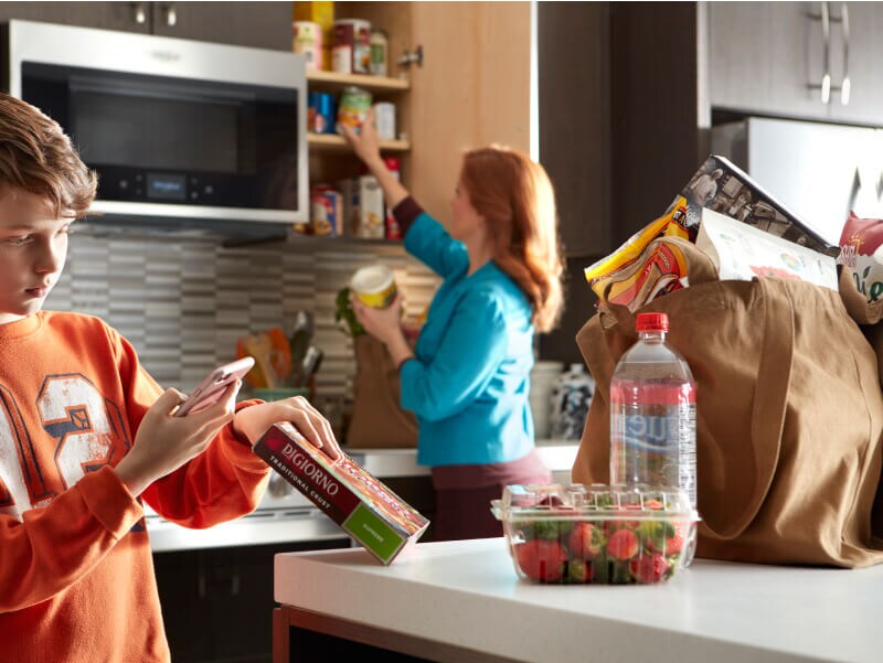 A person scanning a pizza box barcode while a person in the background puts items in the cabinet A person scanning a pizza box barcode while a person in the background puts items in the cabinet