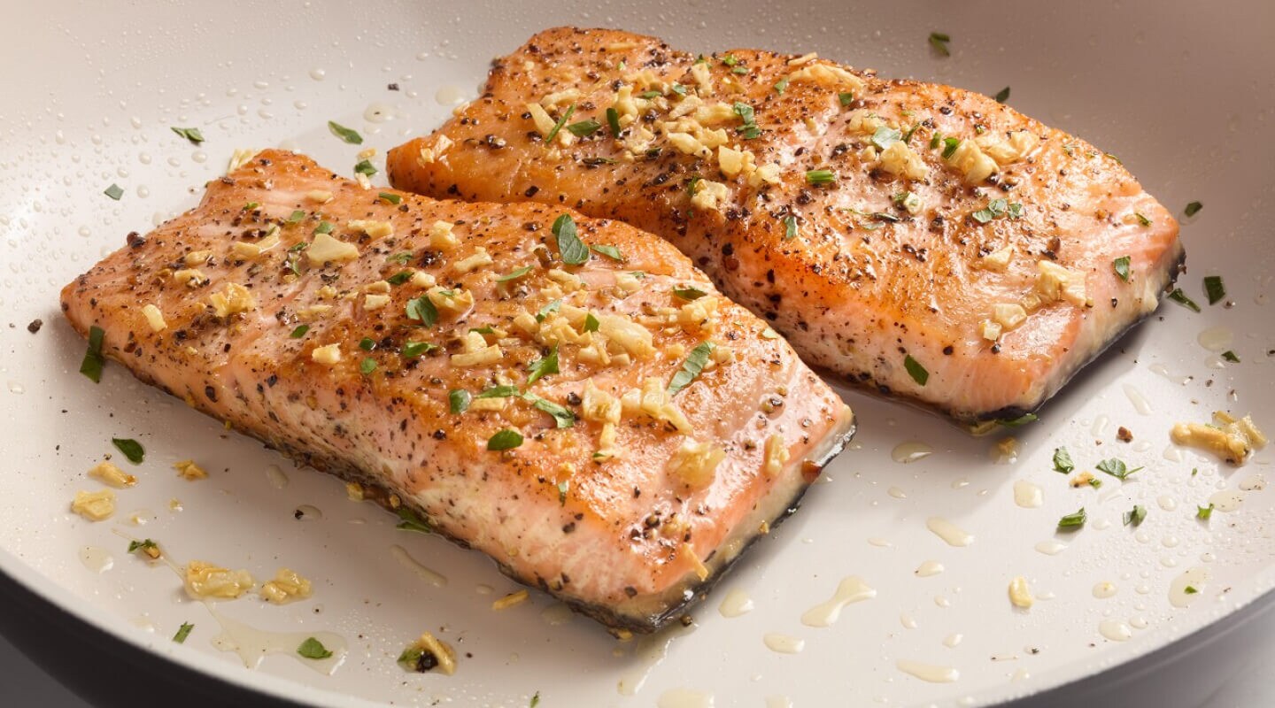 Two pieces of cooked salmon on a white plate