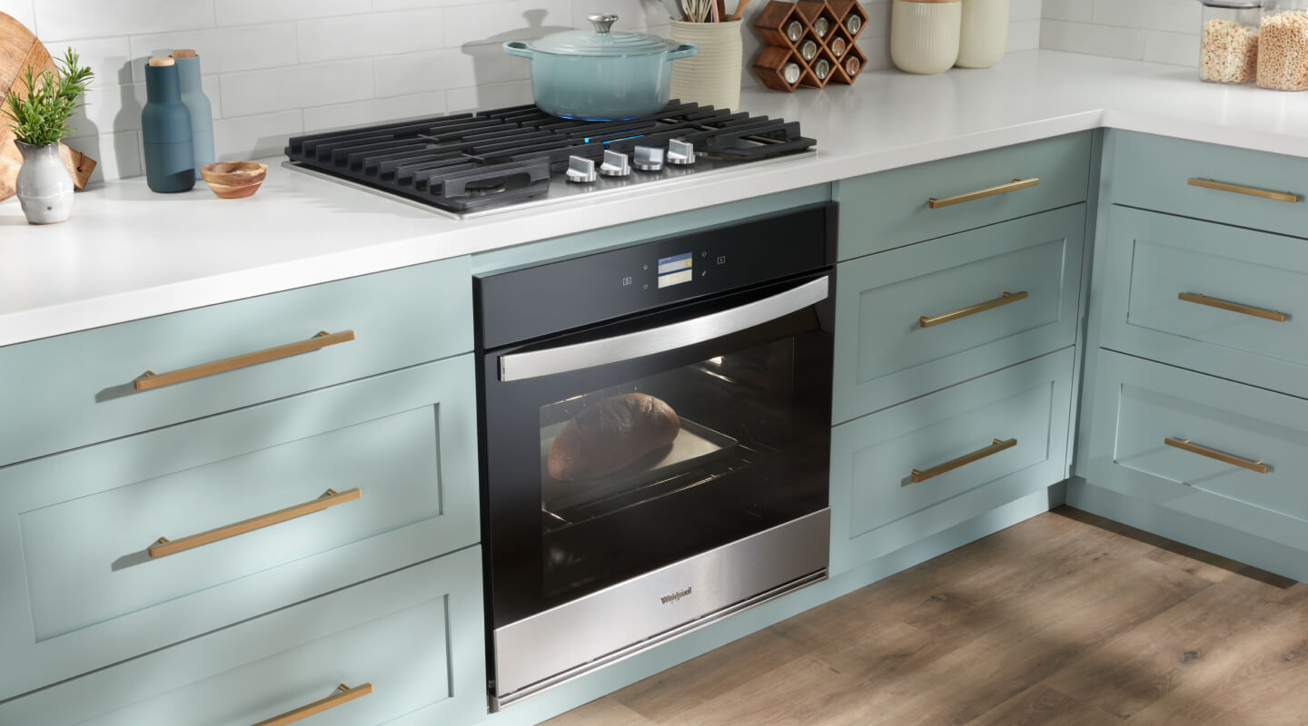 A gas cooktop and a built-in oven placed in a kitchen with sea green cabinets and white countertops