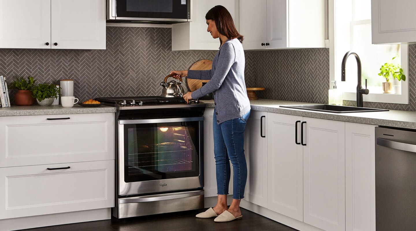 A person placing a tea kettle on the stovetop of a Whirlpool® gas oven in a modern kitchen. A person placing a tea kettle on the stovetop of a Whirlpool® gas oven in a modern kitchen.