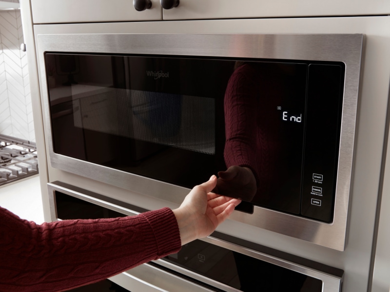 A hand opening a Whirlpool microwave A hand opening a Whirlpool microwave