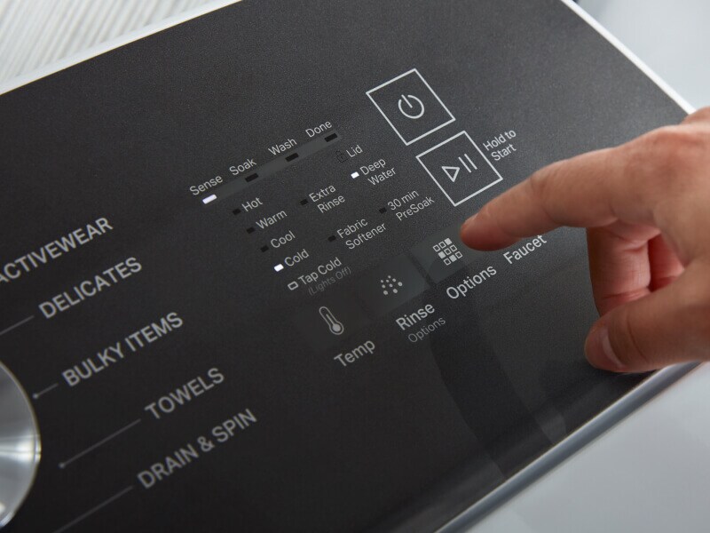 A hand selecting cycle settings on a washing machine control panel A hand selecting cycle settings on a washing machine control panel