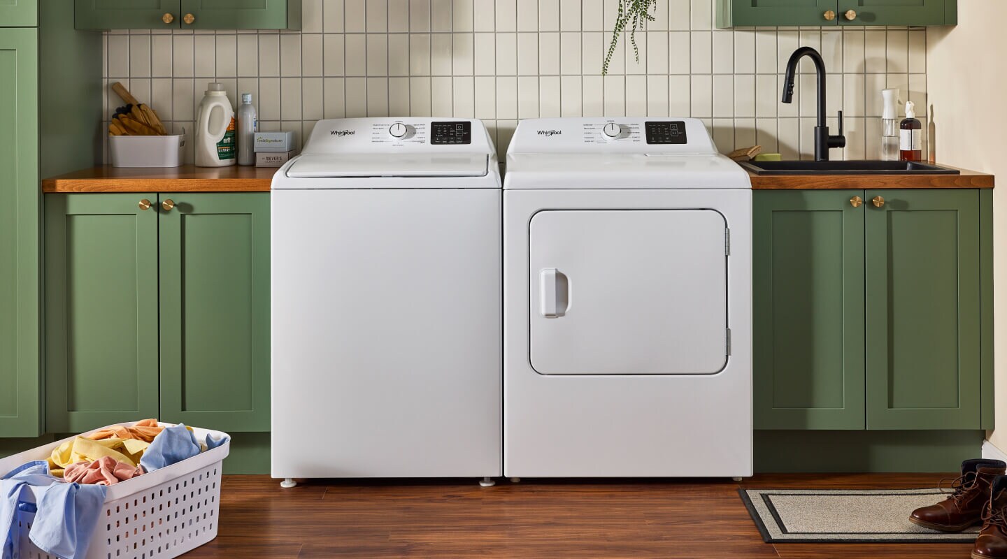 A white side-by-side washer and dryer surrounded by green cabinetry