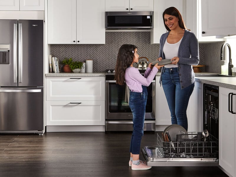 Person handing a child a clean dish next to a dishwasher Person handing a child a clean dish next to a dishwasher