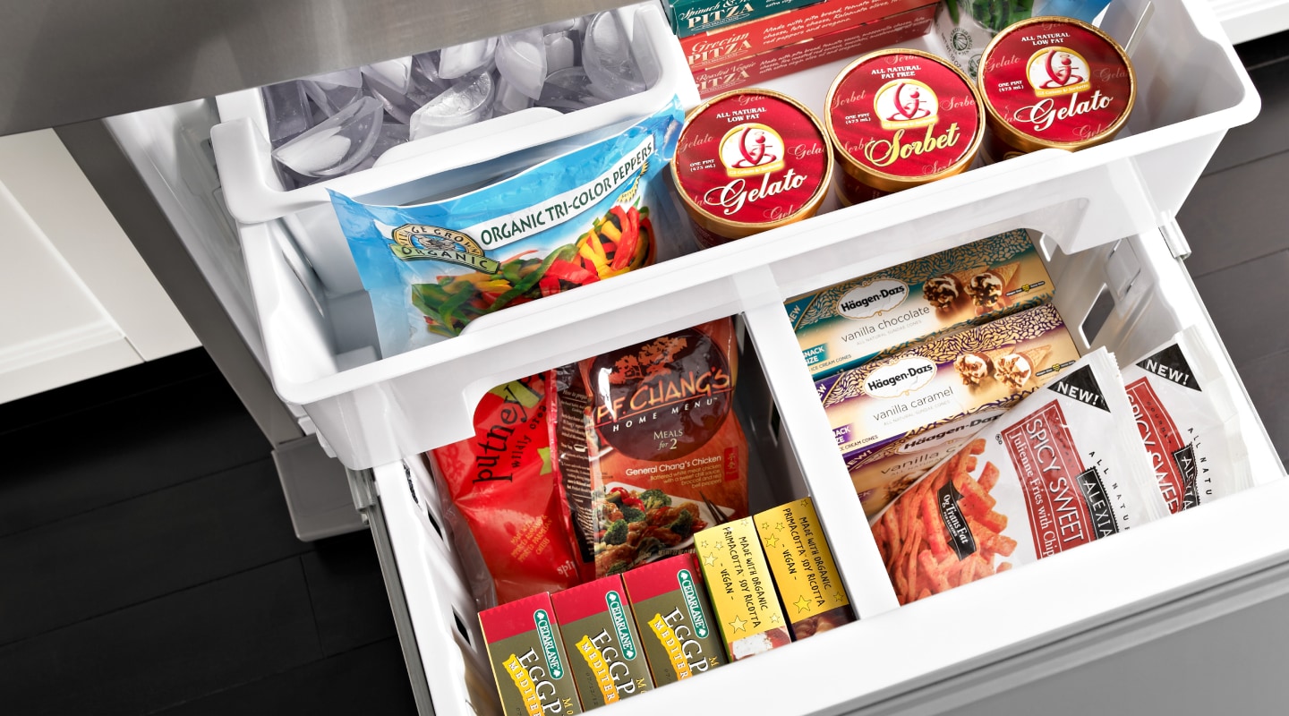 An open bottom freezer drawer holding a variety of frozen groceries