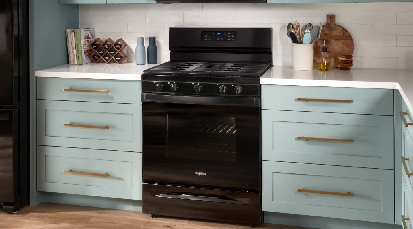 A black gas range between sea green cabinets with white countertops A black gas range between sea green cabinets with white countertops