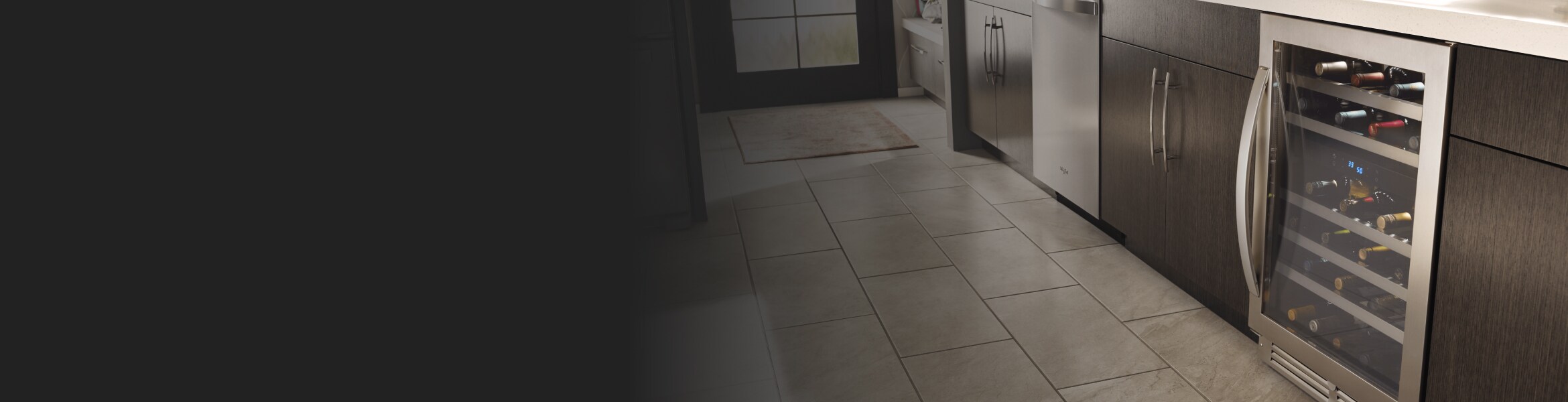 Stocked, under-counter wine refrigerator in kitchen surrounded by brown cabinetry