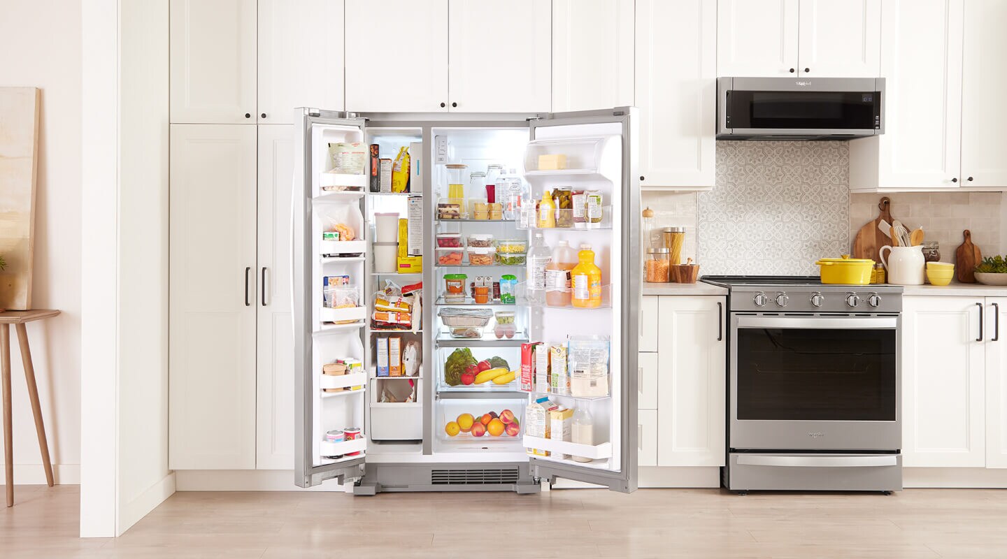 An open refrigerator exposing many containers of food set in an all-white kitchen