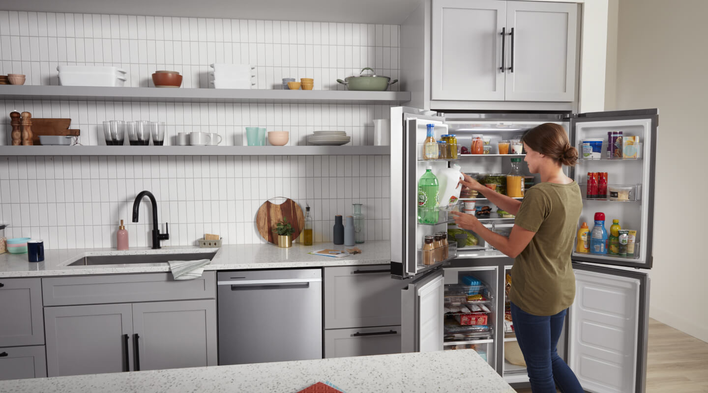 A woman removing a gallon of milk from her open refrigerator in her kitchen