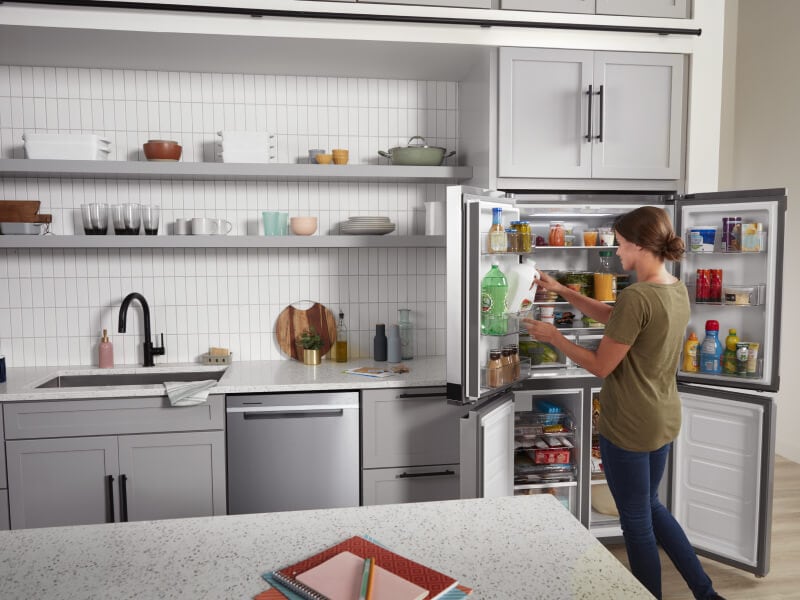 A woman removing a gallon of milk from her open refrigerator in her kitchen