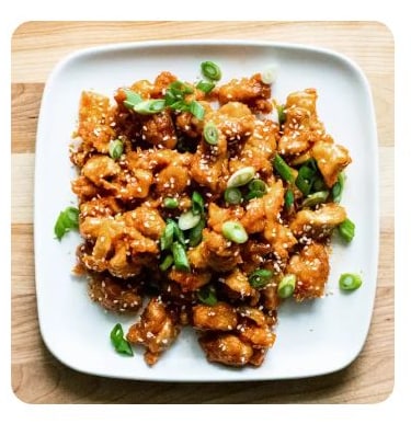 Saucy chicken pieces on a plate with sesame seeds and chopped scallions Saucy chicken pieces on a plate with sesame seeds and chopped scallions